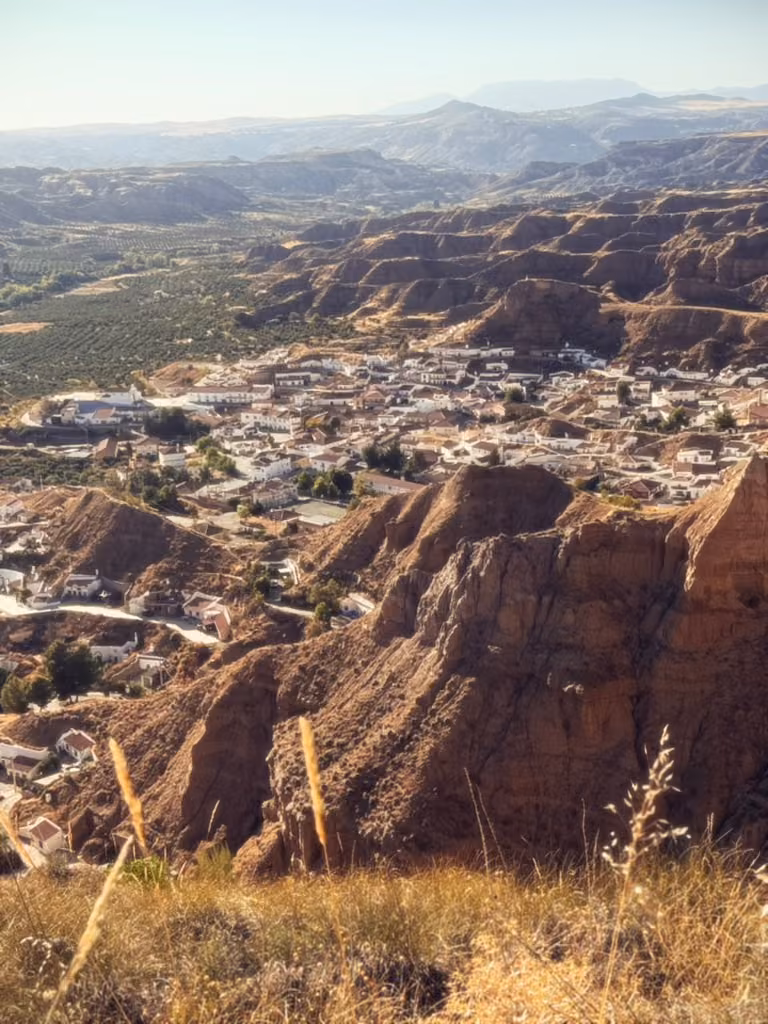 The white houses of Gorafe sit below steep cliffs, with fields and distant hills beyond.