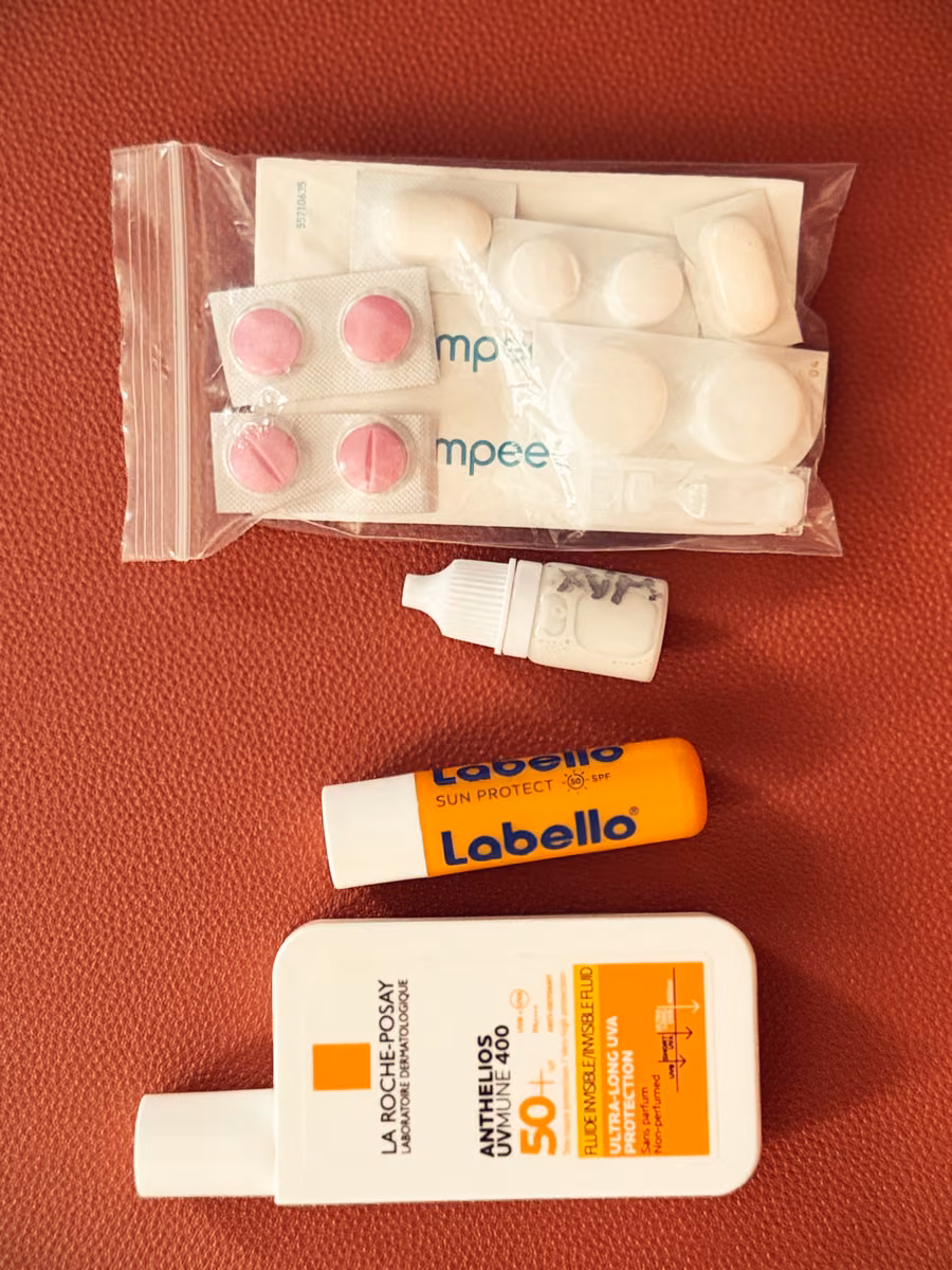 Small packets, lip balm and sunscreen laid out on red upholstery.