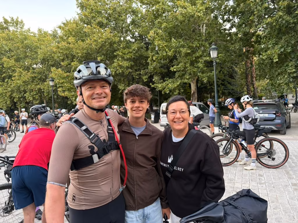 Three people smile together among the riders and loaded bikes in the start square.