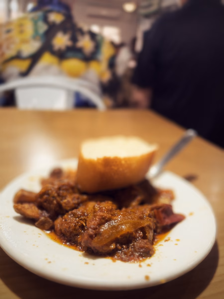 A plate of dark meat stew with onions, a piece of bread on top, on a bar table.